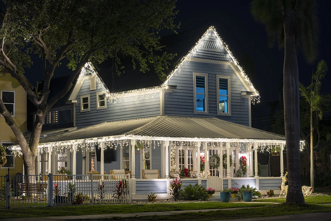 Victorian home with warm white icicle lights along the roofline and porch